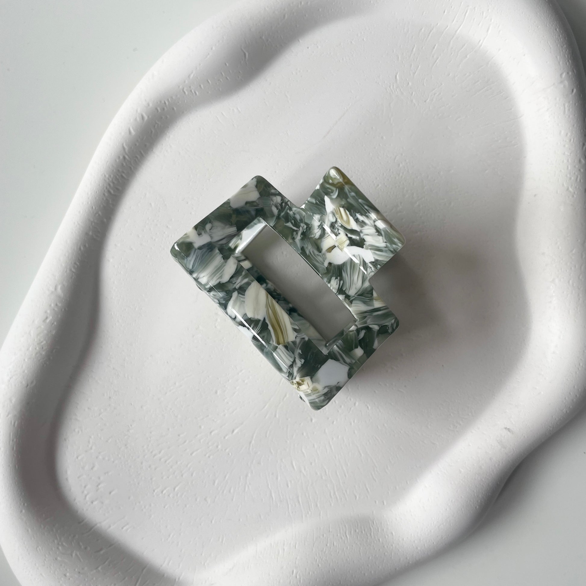 eine mittelgrosse Haarklammer in der Farbe "sage green marble", die auf einem wolkenförmigen und asymmetrischen Schmucktablett liegt